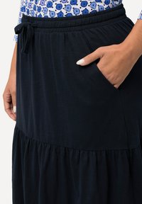 Gonna a strati blu navy realizzata in tessuto morbido. Presenta una cintura elastica con coulisse e tasche laterali per maggiore comodità.