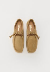 Barna velúr cipők lekerekített orral, bőr fűzőkkel, egyszerű dizájnnal és puha tapintással. Belső részén "Clarks Originals" márkázás található.