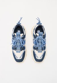 Tenisky s kombinací modrého denimu a síťoviny, krémovými akcenty, zaobleným tvarem, plochými tkaničkami a výrazným nápisem značky po straně.