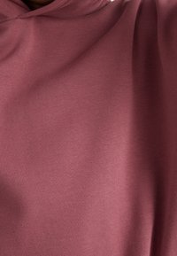 Sudadera con capucha en un color rosa suave, hecha de una tela texturada y suave. Presenta un corte relajado con caídas suaves.