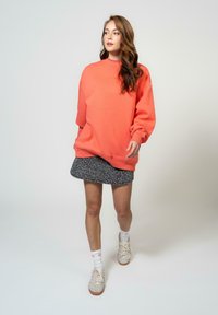 Korallija kreklu ar lielu izmēru un ribotām aprocēm, apvienota ar pelēku leoparda raksta svārku. Modelis valkā baltas zeķes un bežīgas sporta apavus.