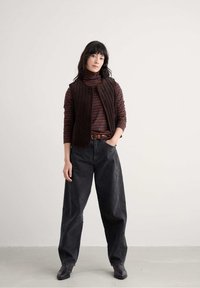 Brūns kordūra veste uz svītrainā turtlenecka, augstā jostasvietā melna plati kāju džinsi un melni potīšu zābaki. Vienkārša, pieguļoša konstrukcija.