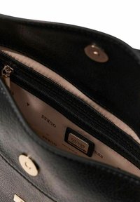 Intérieur d'un sac à main en cuir noir avec une doublure beige, comprenant une poche zippée et une étiquette de marque gravée. Accents de quincaillerie dorée.