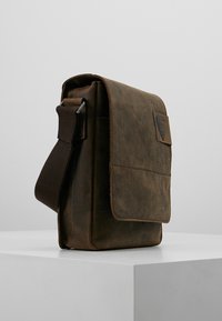 Borsa a tracolla in pelle marrone con una cinghia in tessuto regolabile, chiusura a pattina e superficie textured, caratterizzata da un piccolo dettaglio del logo impresso.