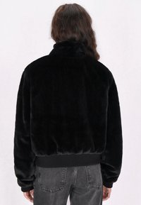 Giacca in ecopelliccia nera con colletto alto, vita elastica e maniche lunghe. Tessuto morbido e design semplice, adatta per un abbigliamento informale.