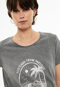 Camiseta de algodón gris de manga corta con un gráfico blanco de un sol, una palmera y olas, etiquetado "CARTA POSTAL DEL PARAÍSO."