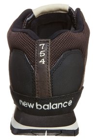 Sneaker New Balance nero e marrone con materiali in rete e sintetici, dotato di un'apposita linguetta sul tallone e logo bianco sul tallone. Modello 754.