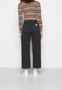 Schwarze weite Jeans mit zwei Gesäßtaschen und einem weißen Logo-Tag, kombiniert mit einem mehrfarbigen gestreiften Langarmshirt und weißen Sneakers.