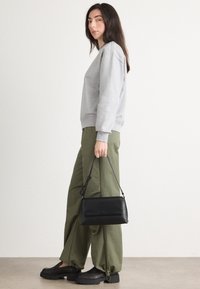 Μαύρη δερμάτινη τσάντα με αποσπώμενο λουρί, φορεμένη με γκρι φούτερ και ελβετό πράσινο παντελόνι. Μαύρες πλατφόρμες ολοκληρώνουν το λουκ.