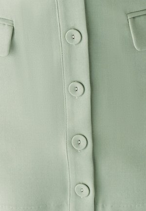 Svetlo zelena tkanina z gladko teksturo, z obrobnimi krožnimi gumbi in dvema žepoma na prsih. Enostavna zasnova s gumbi.