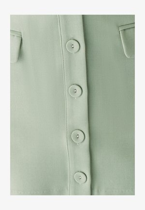 Light green fabric with a smooth texture, featuring six round buttons and two chest pockets. Simple, button-down shirt design.