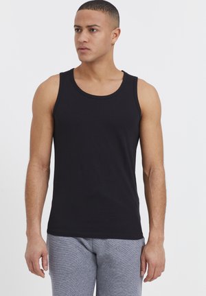 Débardeur en coton noir à col rond, avec une coupe slim. Porté avec un pantalon de jogging gris chiné. Texture lisse.