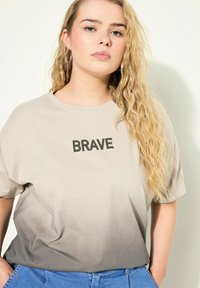Svetle šedé tričko s nápisem "BRAVE" v tučných černých písmenech. Tričko má ombre efekt, který přechází do tmavší šedé.