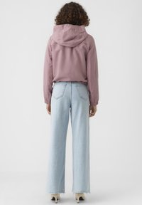 Light pink hooded jacket with elastic cuffs, paired with high-waisted, wide-leg light blue jeans featuring a frayed hem and back pockets.