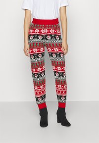Calças com padrão vermelho, preto e verde, apresentando bonecos de neve, flocos de neve e árvores. Material macio, cintura elástica, corte ajustado, combinadas com botas pretas.