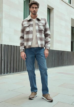 Plaid wool jacket with cream faux fur collar, beige sweater, and blue jeans. Brown and white sneakers complete the outfit.