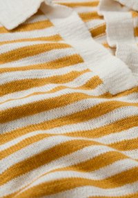Polo en tricot aux rayures horizontales jaunes et blanches. Présente un tissu texturé et un col avec un léger détail volanté.