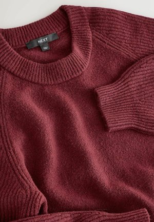Burgundy stickad tröja med rund halsringning och ribbade muddar. Mjuk textur, med horisontell ribbning längs axlarna och ärmarna.