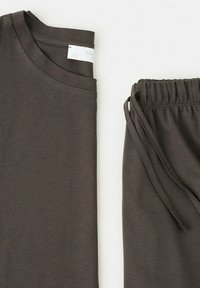 Foldet mørkegrå T-shirt med korte ærmer og matchende bukser med snor på en lys baggrund.