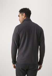 Pull g Gray foncé avec un col haut et un tissu texturé. Il possède des manches longues et un ourlet légèrement arrondi. Détails de couture subtils visibles.