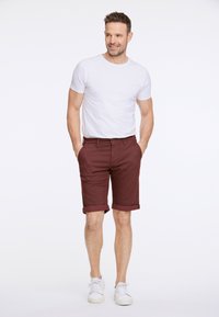 Burgundryfärgade shorts med uppvikt fåll, kombinerade med en enkel vit t-shirt och vita sneakers. Tyget verkar slätt och lätt.