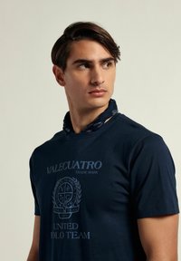 Camiseta azul marino con estampado de logo que incluye el texto "VALECUATRO" y "UNITED POLO TEAM". Mangas cortas y escote redondo. Tejido de algodón texturizado.
