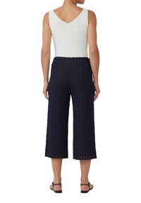 Marineblauwe culotte broek met een gestructureerd, geweven patroon, voorzien van een brede pijp en een elastische tailleband. Gecombineerd met een witte mouwloze top.
