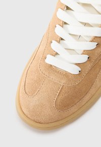 Beige semsket-sneakers med hvite snører, rund tå, teksturert overflate og gummisåle. Designet har subtile sømdetaljer.