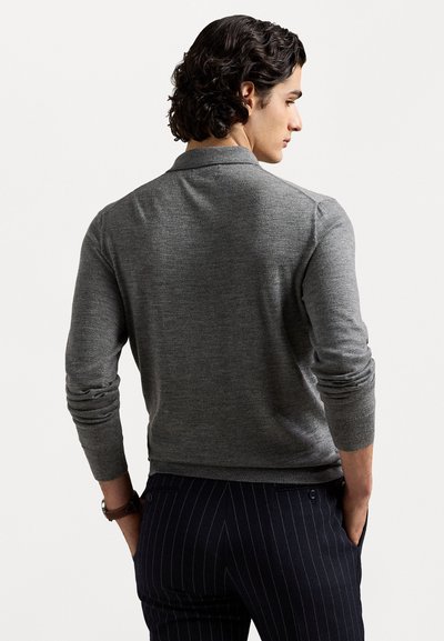 Pilkas megztas puloveris su ilgomis rankovėmis ir apykakle, pasižymintis glotniu tekstūru. Derinama su tamsiomis dryžuotomis kelnėmis.