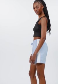 Un crop top noir et un short bleu clair avec des rayures blanches sur les côtés. Le short a une taille élastique et un cordon de serrage.