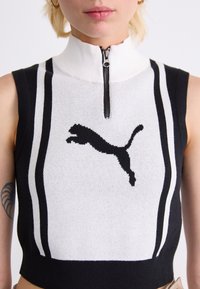 Svart och vit ärmlöst stickad topp med hög krage, en fjärdedels dragkedja och en framträdande svart Puma-logotyp.