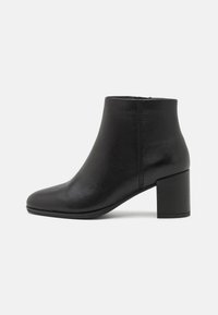 Botín negro de cuero hasta el tobillo con punta redondeada, textura suave y tacón cuadrado. Presenta una costura mínima y un diseño elegante y moderno.