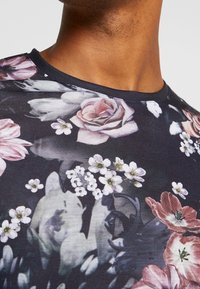 Camiseta negra de manga corta con estampado floral, que presenta rosas rosas y flores blancas, con una textura de tela suave y un cuello redondo.