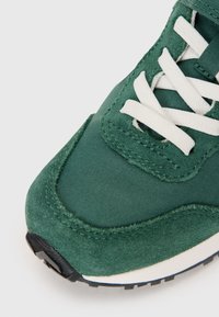 Πράσινα σουέτ και υφασμάτινα sneakers με λευκές κορδόνες, υφαντή επιφάνεια, στρογγυλή μύτη και μαύρη σόλα. Ορατή ενισχυμένη ραφή.