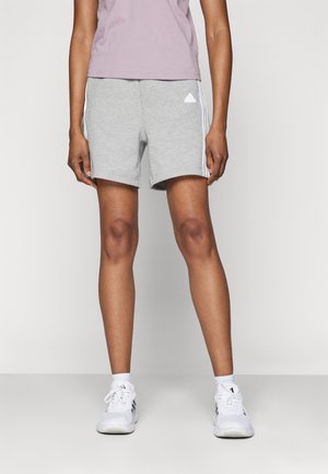 Pantalones cortos de mezcla de algodón gris con rayas laterales blancas y detalle de logo triangular. Combinados con zapatillas deportivas blancas y calcetines hasta el tobillo.