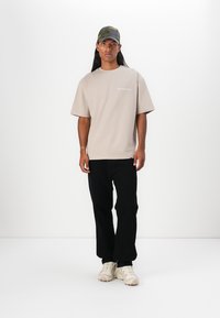 Beige bomulds t-shirt med korte ærmer og rund halsudskæring. Sammen med sorte bukser og cremefarvede sneakers. Camouflage kasket bæres.
