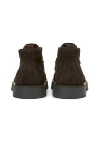 Bottines en cuir suédé marron avec une texture mate, un talon arrondi et un détail de tirette. Conçues avec des coutures renforcées et une épaisse semelle en caoutchouc noir.
