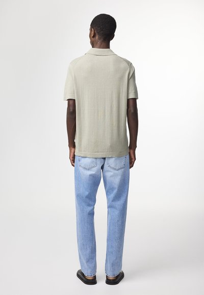 Polo shirt verde chiaro a maniche corte, tessuto traspirante, vestibilità rilassata, abbinato a jeans blu chiaro a gamba dritta e sandali neri flat.