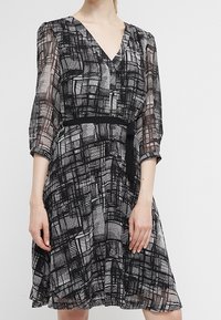 Abito a fantasia in bianco e nero con scollo a V, maniche a tre quarti, vita cintrata e gonna fluente. Realizzato in tessuto leggero e trasparente.