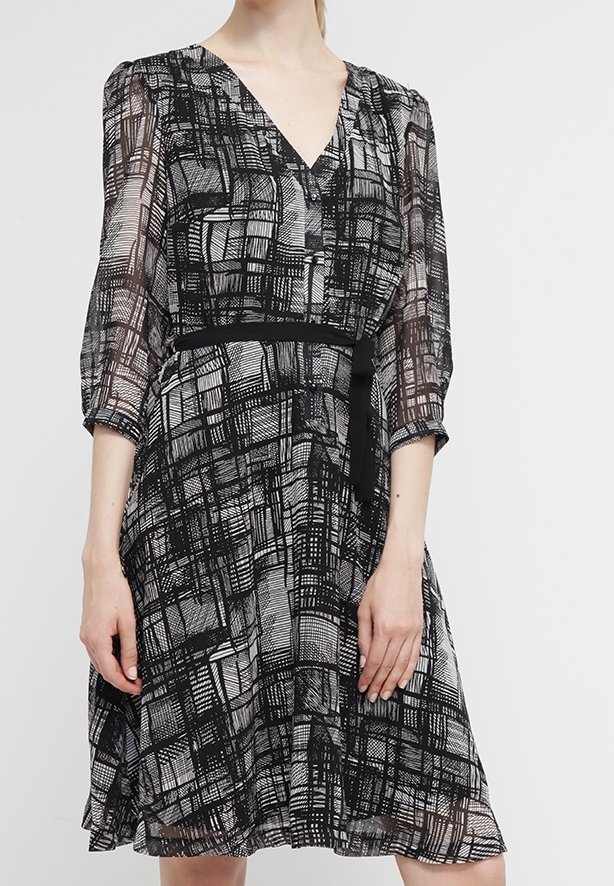 Abito a fantasia in bianco e nero con scollo a V, maniche a tre quarti, vita cintrata e gonna fluente. Realizzato in tessuto leggero e trasparente.