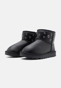 Bottes noires à la cheville en cuir synthétique, avec des accents de œillets sur le haut et une semelle en caoutchouc texturé. Design à bout rond.