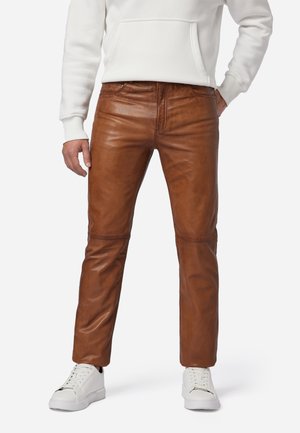 Bruine leren broeken met een gladde textuur, met een recht gesneden ontwerp en zichtbare stiksels, gecombineerd met witte sneakers.