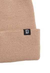 Puha, világos rózsaszín anyagból készült kötött sapka hajtott szegéllyel. Oldalán fekete címkét visel, amelyen fehér "B" betű látható.
