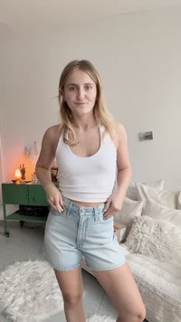 Balta bezpiedurņu blūze un gaiši zila džinsu šorti. Šorti ir ar augstu vidukli un brīvu piegriezumu, tiem ir priekšējā pogu aizdare un sarullēti malām.