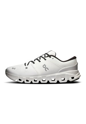 Scarpa sportiva bianca con lacci bianchi e neri, tomaia in mesh traspirante e suola spessa segmentata progettata per ammortizzazione e supporto.