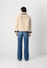 Leren schapenvacht jack in crème met zwarte accenten, met een kraag en opgerolde mouwen, gecombineerd met hoge taille wijd gesneden blauwe jeans.