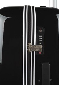 Maleta rígida negra con rayas blancas, cierres dobles, cerradura de combinación y característica de cerradura de viaje aprobada por la TSA. Acabado suave y brillante.