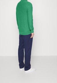 Grön stickad tröja med ståkrage, kombinerad med marinblå byxor och vita sneakers. Har en strukturerad yta och åtsittande cuffs.