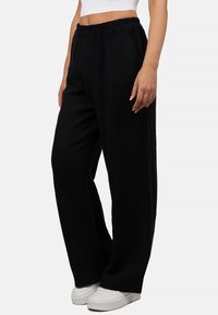 Zwarte wijde broek gemaakt van een textuurstof met een elastische tailleband. Gecombineerd met witte sneakers voor contrast.