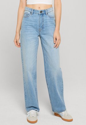 Világoskék, magas derekú, egyenes szárú farmer enyhe kifakulással, öt zsebes kialakítással és gombos záródással. Fehér tornacipővel viselve.